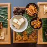 A top-down view of tofu and tauhu on a wooden table, showing different textures and preparations in an Asian culinary setting.